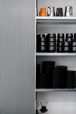 Minimalistische opbergkast van Dune, de kast is half open waardoor je de mat zwarte kopjes gedeeltelijk kan zien
