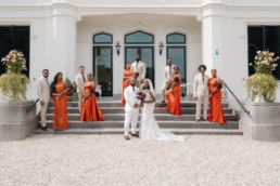 Bruiloft groepsfoto, koppels in wit en oranje voor een mooi herenhuis