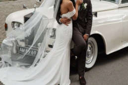 Echtpaar poseert naast een klassieke rolls royce, witte trouwauto